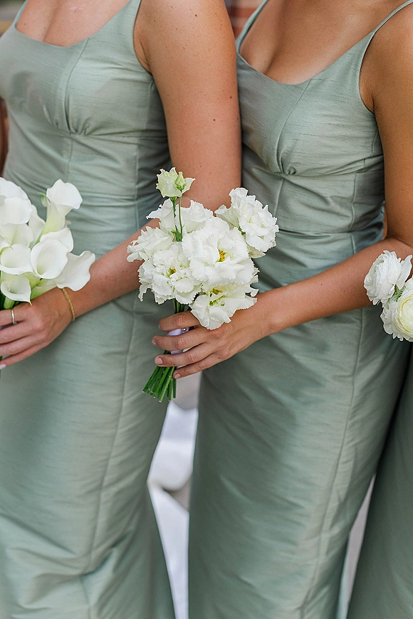 Bridesmaid dresses in sage green bridesmaid dresses with white calla lily bouquets, ribbon wrap and gold bracelet by a brick wall