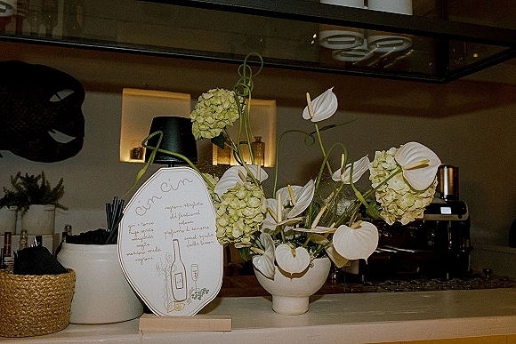 Wedding bar decor with a wedding cocktail menu sign beside white anthurium and green hydrangea in a ceramic vase on the bar counter