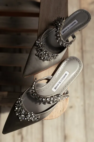 Bridal shoes with rhinestone embellishments on pointed toe mule heels, resting on a wooden bench over a wood floor