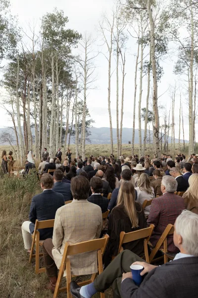Wedding ceremony in an aspen grove with outdoor wedding ceremony seating, guests on wood folding chairs facing the couple in a meadow with mountain views