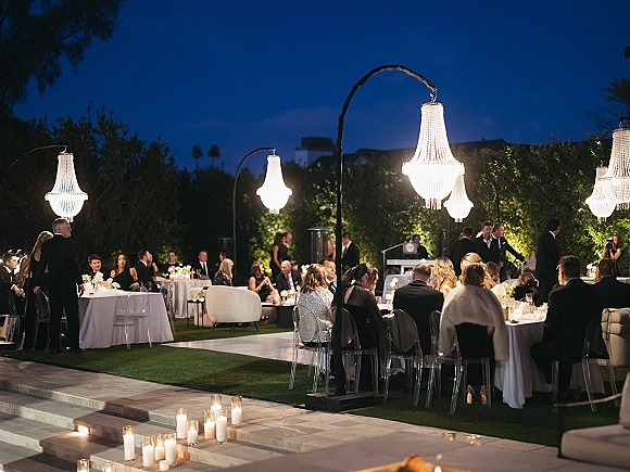 Outdoor wedding reception with garden reception lighting, chandeliers over round tables, candles on patio steps, and lounge seating at night