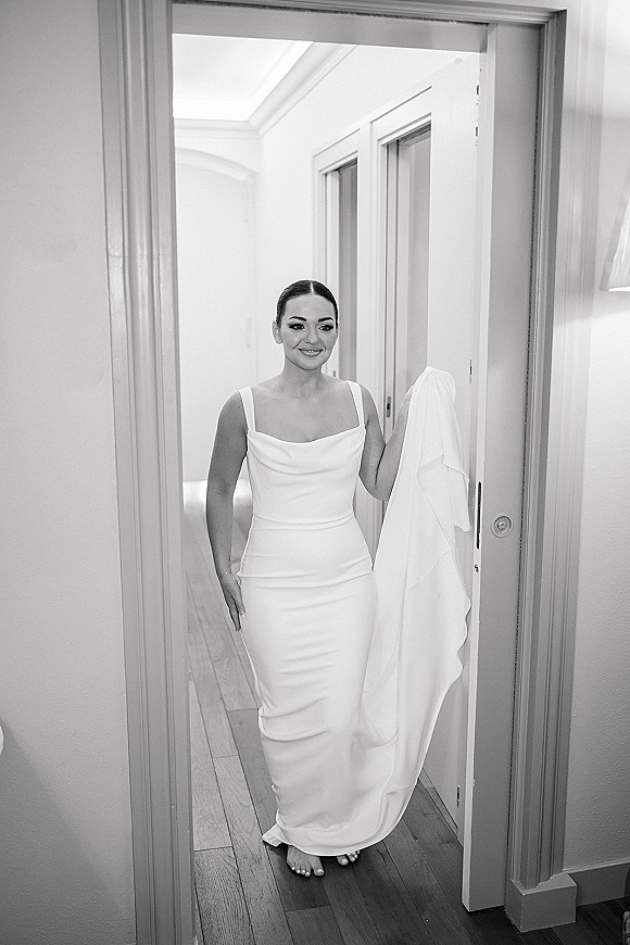 Bridal portrait of a bride in a strapless wedding dress, holding her train in a doorway of an elegant indoor hallway with wood floors