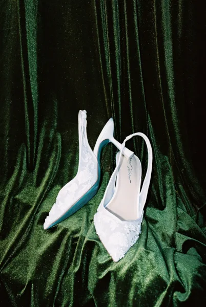 Bridal shoes, lace wedding shoes in white lace slingback heels with floral appliqué and pointed toes on draped green velvet fabric