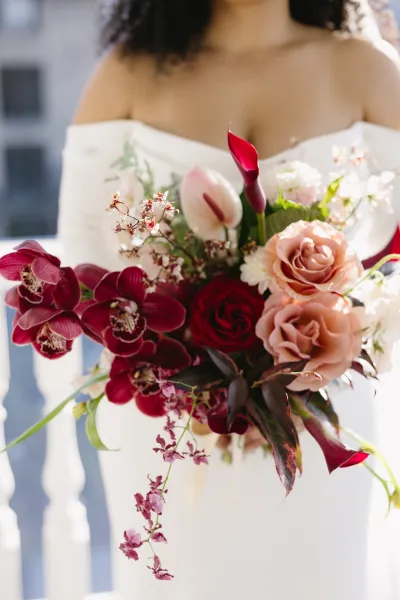 Bridal bouquet, burgundy and blush bouquet with calla lilies, orchids, roses and tulips, held before a white railing in outdoor light