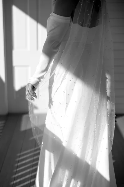 Wedding dress detail showing a strapless wedding dress with pearl veil, long bridal gloves, and ring in soft window light indoors