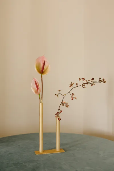 Minimalist wedding centerpiece with a gold bud vase holding pink anthurium and an orchid branch on a round table against a neutral wall