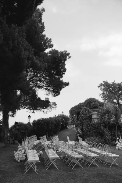 Outdoor ceremony setup with white folding chairs lining a garden wedding ceremony aisle, floral markers and lanterns on a lawn path