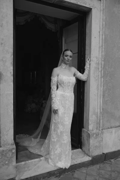 Bridal portrait in a lace long sleeve wedding dress with cathedral veil, standing in a stone doorway with deep interior shadows behind