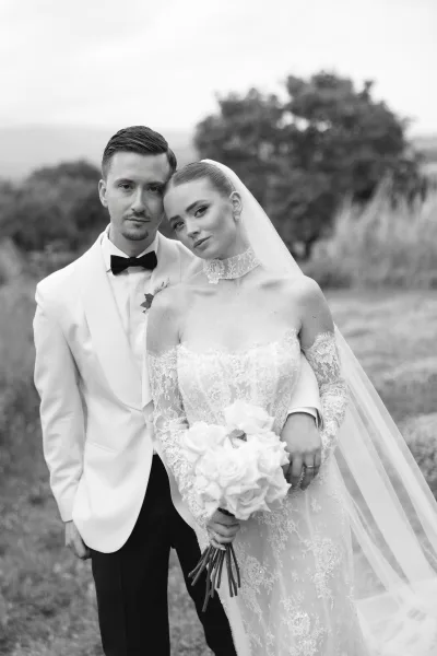 Couple portrait in a black and white wedding portrait, bride leaning on groom with rose bouquet and veil in an open field backdrop