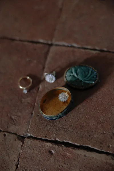 Wedding rings in a velvet ring box, featuring a gold wedding band and diamond engagement ring on a terracotta brick floor