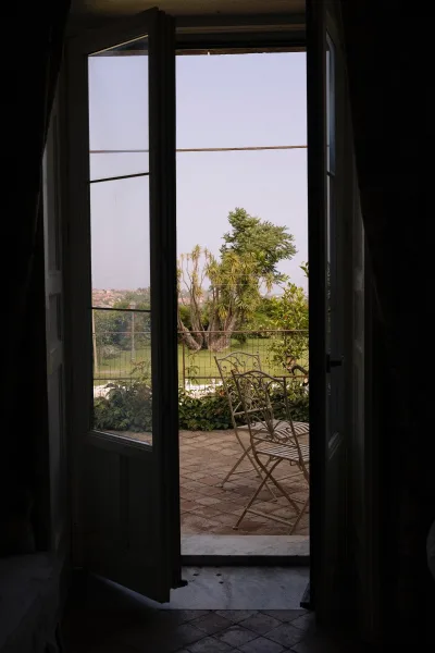 Wedding venue view through open glass doors with sheer curtains, wrought iron patio seating on a brick terrace overlooking gardens and distant town