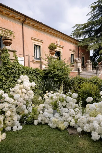Wedding floral installation with grounded wedding florals of white roses and hydrangeas lining stone steps by an ivy-covered villa terrace