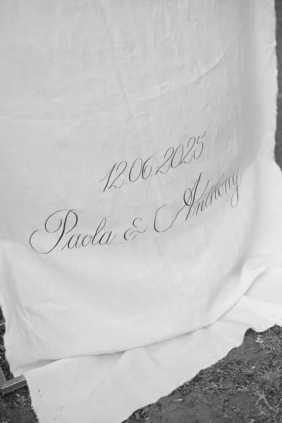 Wedding signage with calligraphy wedding sign text on a fabric drape, laid on grass for a simple black-and-white welcome display