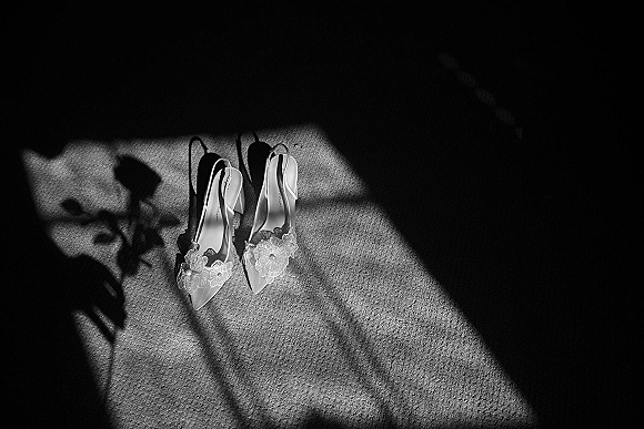 Bridal shoes with lace wedding heels featuring floral appliqué and ankle straps, resting on carpet in window light shadows