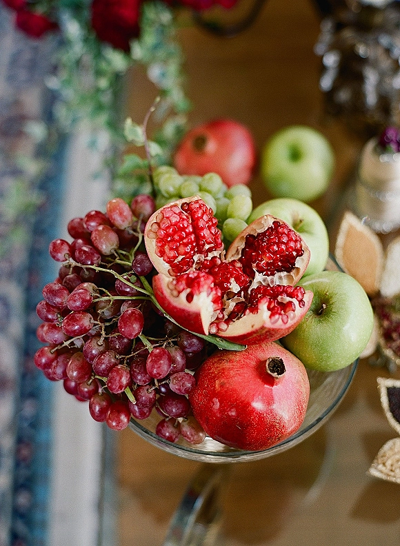 Fruit centerpiece with a pomegranate centerpiece mix of grapes and apples in a glass bowl, paired with florals on a wood table setting