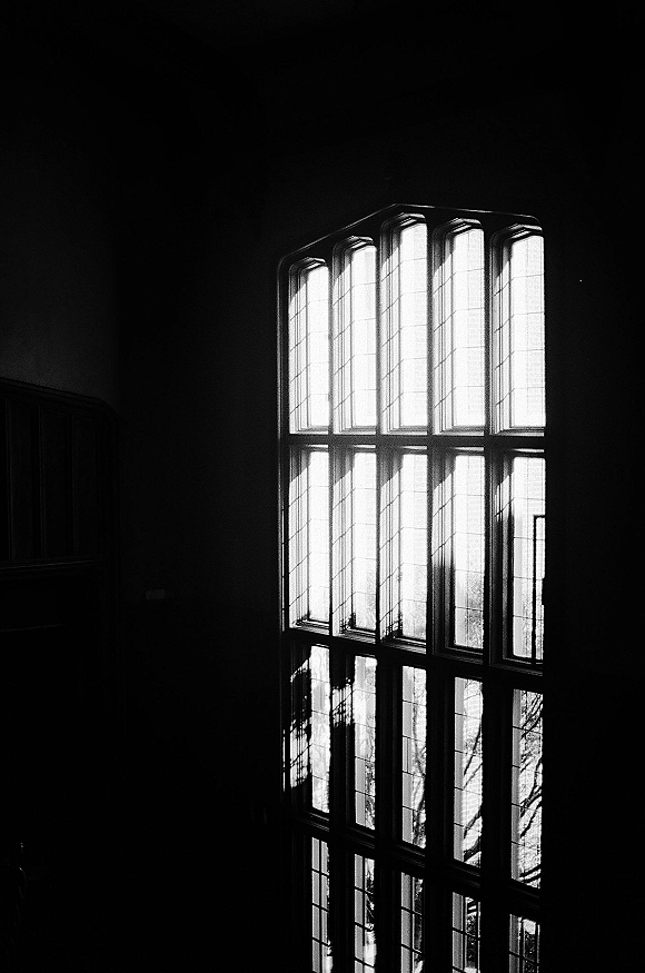 Wedding venue windows with church window light casting dramatic shadows on a dark interior wall, trees silhouetted beyond tall panes