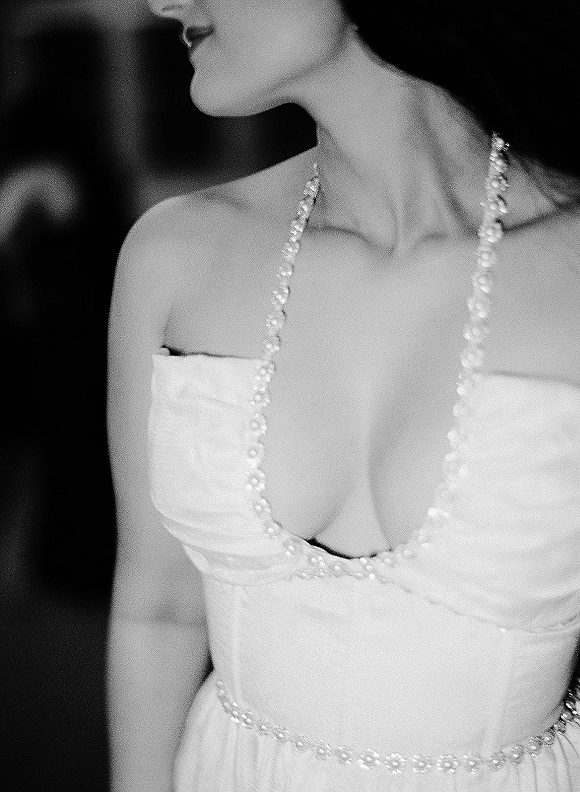 Wedding dress close-up showing a strapless wedding dress with pearl trim and corset bodice, paired with a pearl necklace against a dark indoor backdrop