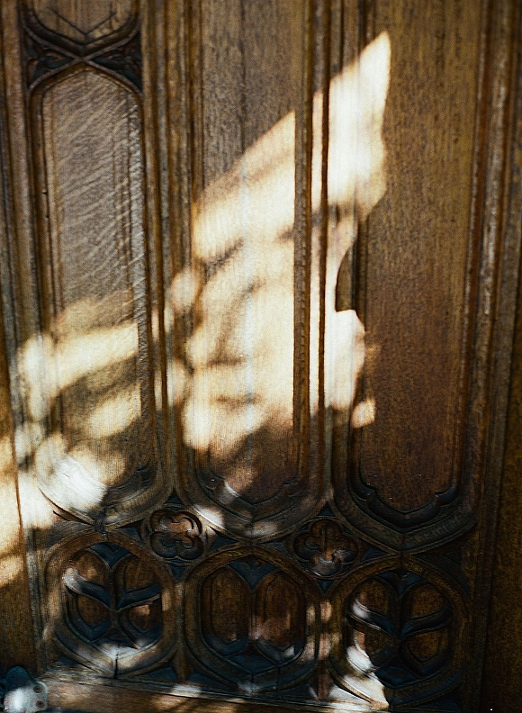 Groom silhouette in dramatic sunlight shadows on a carved wooden door, creating a moody wedding day portrait before the ceremony