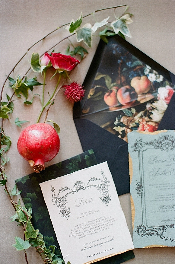 Invitation suite wedding invitation flat lay with black envelopes, deckle-edge gold paper, ivy vine, rose and pomegranate on neutral fabric background