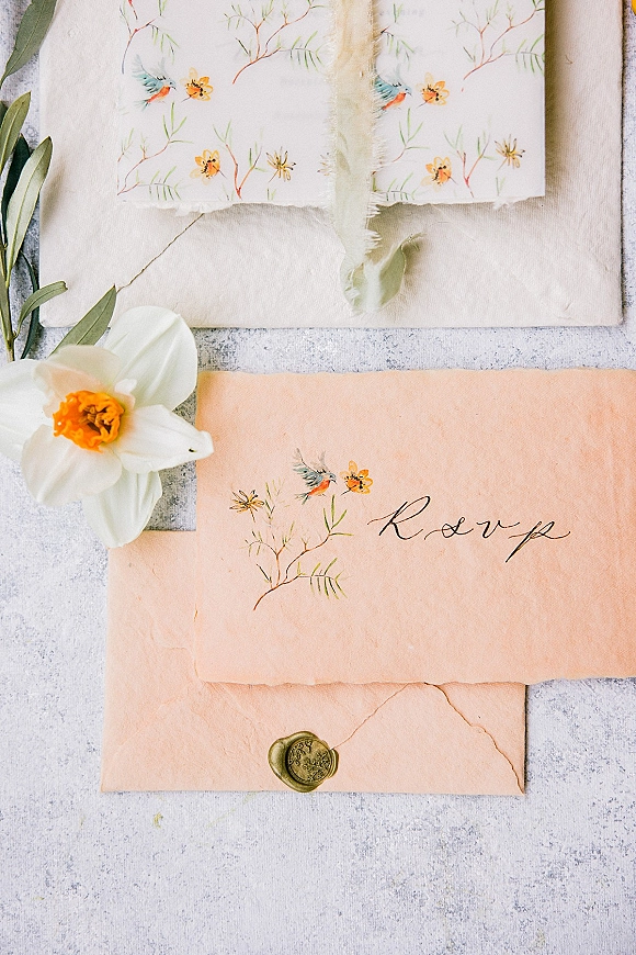 Wedding invitation suite with wax seal envelope, calligraphy and watercolor florals, styled on stone and linen with daffodil sprigs