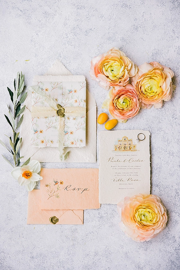 Invitation suite wedding invitation flat lay with vellum wrap and wax seal, deckled edge paper, ring and ranunculus on gray surface