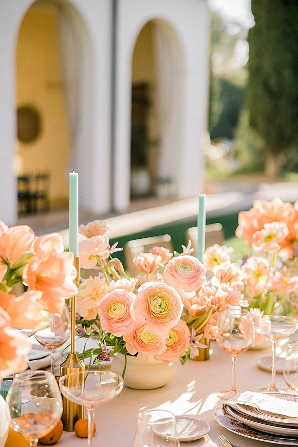 Reception tablescape with peach wedding tablescape florals, pastel taper candles in brass holders, citrus accents, on an outdoor patio with white arches