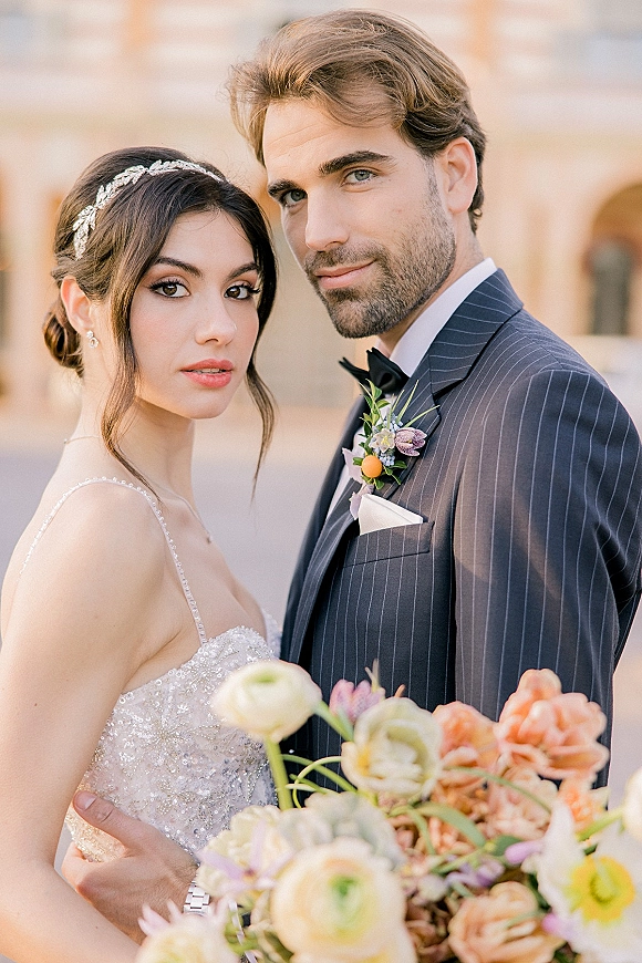 Couple portrait of bride and groom close up, bride looking at camera while holding bouquet in a stone courtyard with arches