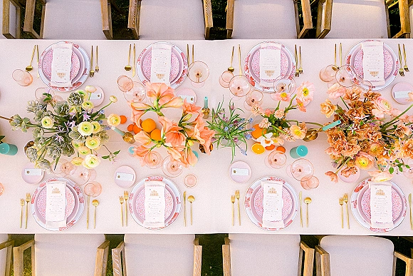 Reception tablescape shown in a top view wedding table arrangement with pink linens, floral centerpieces, gold flatware, and taper candles on a lawn