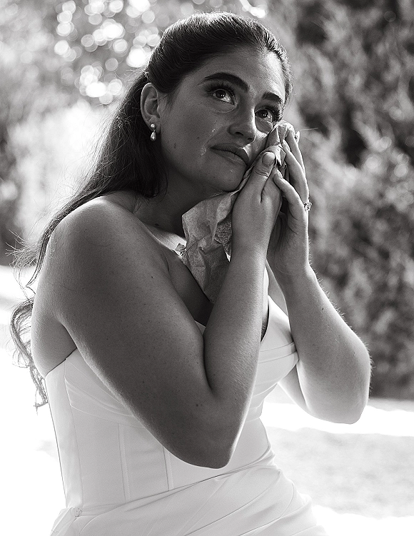 Emotional bride portrait of a bride wiping tears with a handkerchief, wearing pearl drop earrings and strapless dress in sunlit greenery