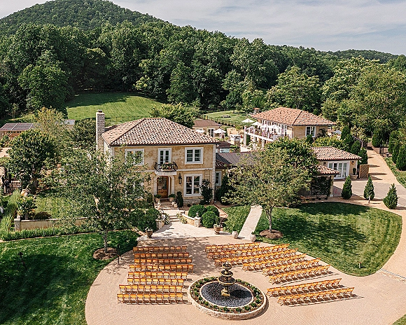 Ceremony setup with outdoor wedding ceremony seating in wood chairs around a fountain on stone pavers in a villa courtyard garden