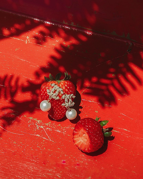 Wedding earrings with pearl drop crystals beside strawberries on a red painted wood surface with soft leaf-shadow accents