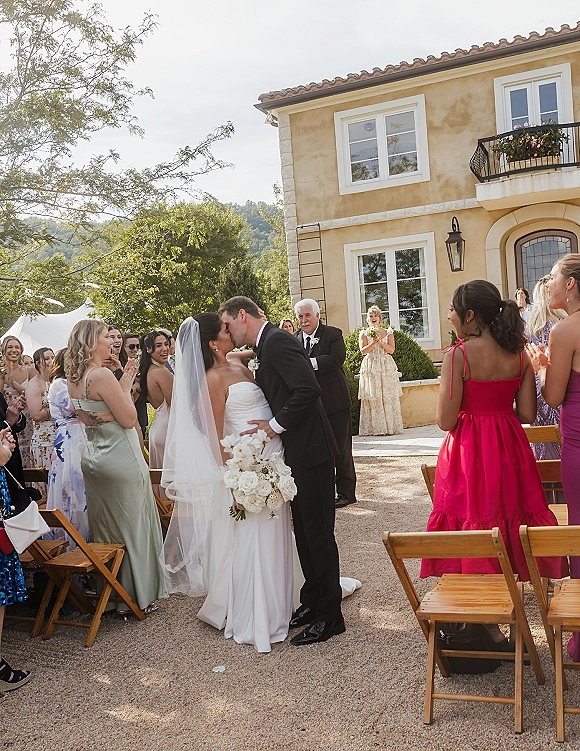 Ceremony kiss moment with wedding ceremony kiss as the bride and groom embrace, guests applaud in a villa courtyard aisle with hills behind