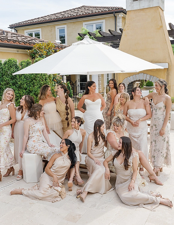 Bridesmaids group photo of the bride with bridesmaids in mixed dresses, seated on a villa patio with greenery, under an umbrella