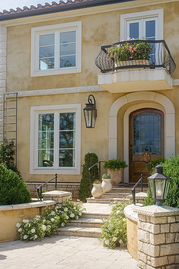 Wedding entrance decor with front door wedding flowers lining stone steps, white florals and greenery garlands on wrought iron railings by lanterns