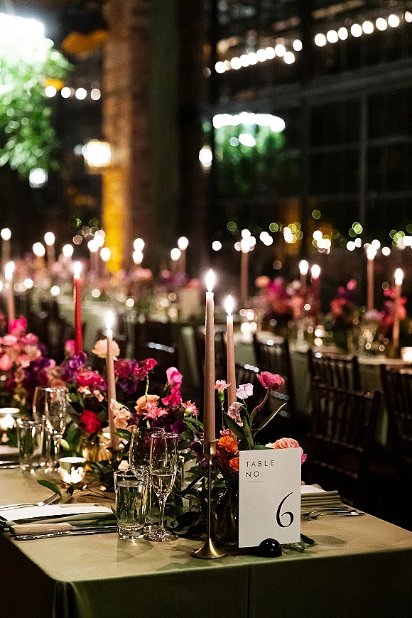 Reception tablescape with wedding reception table decor, brass candlesticks and taper candles, floral centerpieces, and string lights on an outdoor patio at night