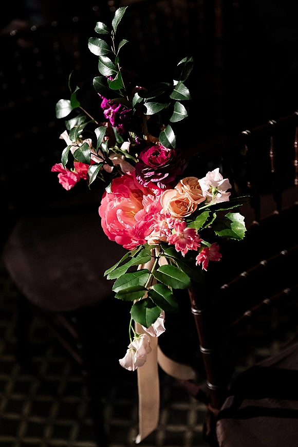 Aisle chair flowers with a wedding chair flowers posy of roses, peony, and greenery tied with ribbon in a dark indoor venue