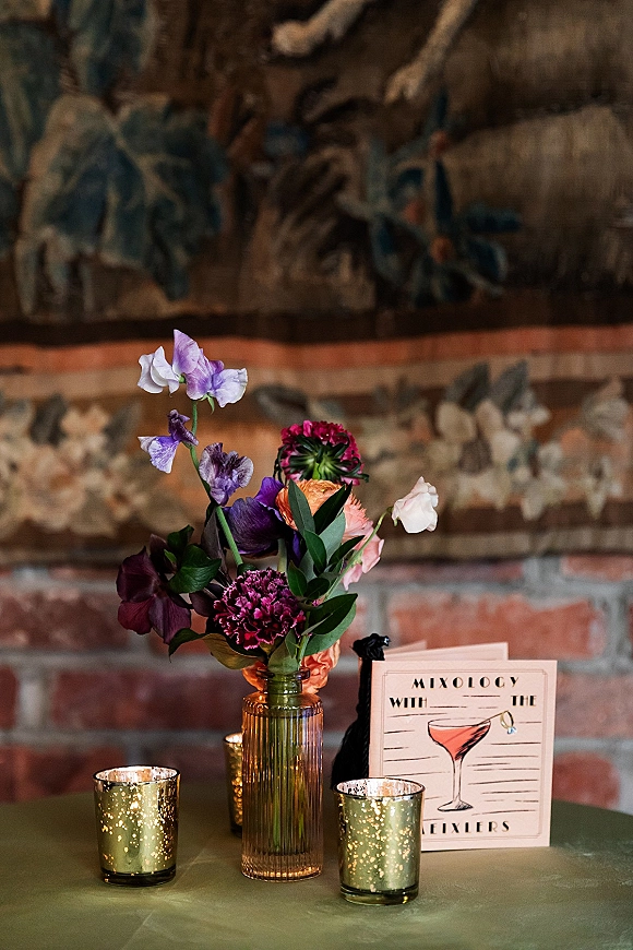 Cocktail table decor with a wedding cocktail hour table sign, small floral centerpiece in a glass vase and votive candles on velvet cloth indoors