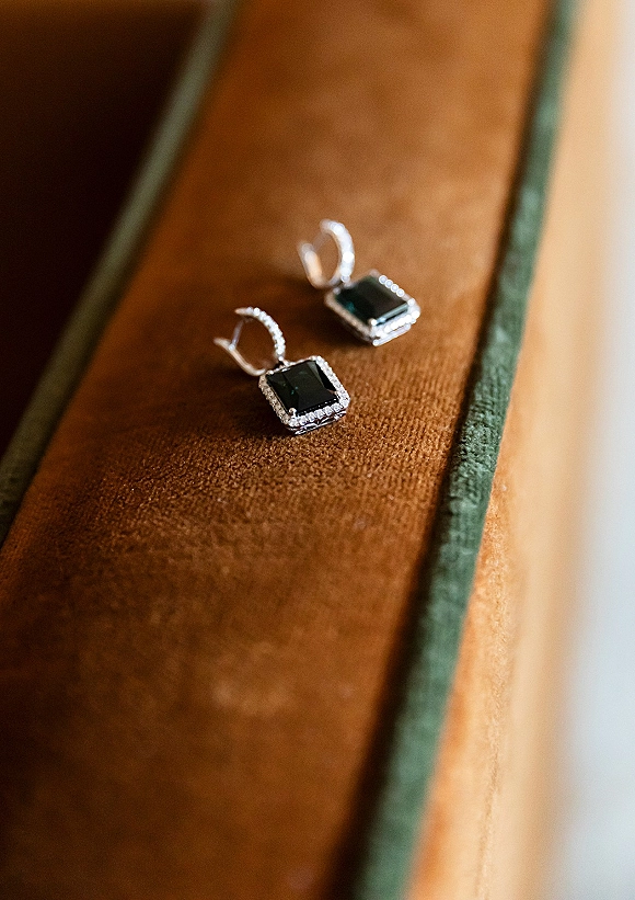 Wedding earrings with black gemstone halo in silver pavé setting resting in a velvet ring box on a brown velvet surface