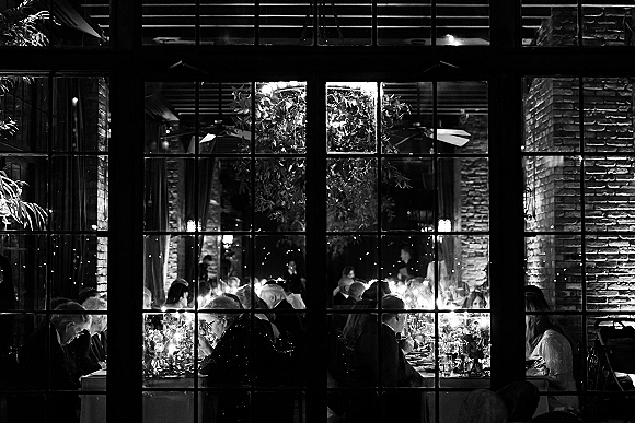Wedding reception dinner with a candlelit wedding reception banquet table, floral centerpieces and place settings beside brick walls and windows at night