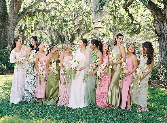 Bridesmaid group photo with bride and bridesmaids in satin dresses holding calla lily bouquets under oak trees with hanging moss