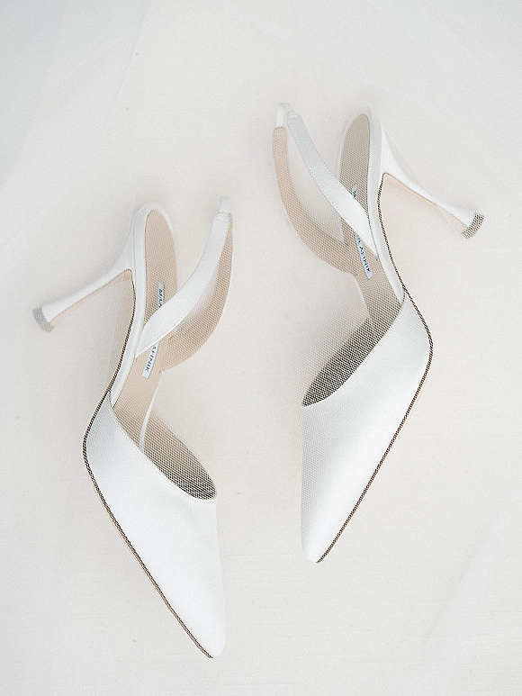 Bridal shoes, white wedding heels in a flat lay with pointed-toe slingback straps resting on a soft white fabric surface