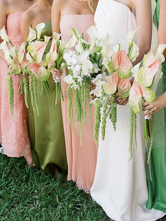 Bridesmaid bouquets with tropical wedding bouquet blooms like calla lilies and orchids, held by bridesmaids on a grass lawn with greenery accents