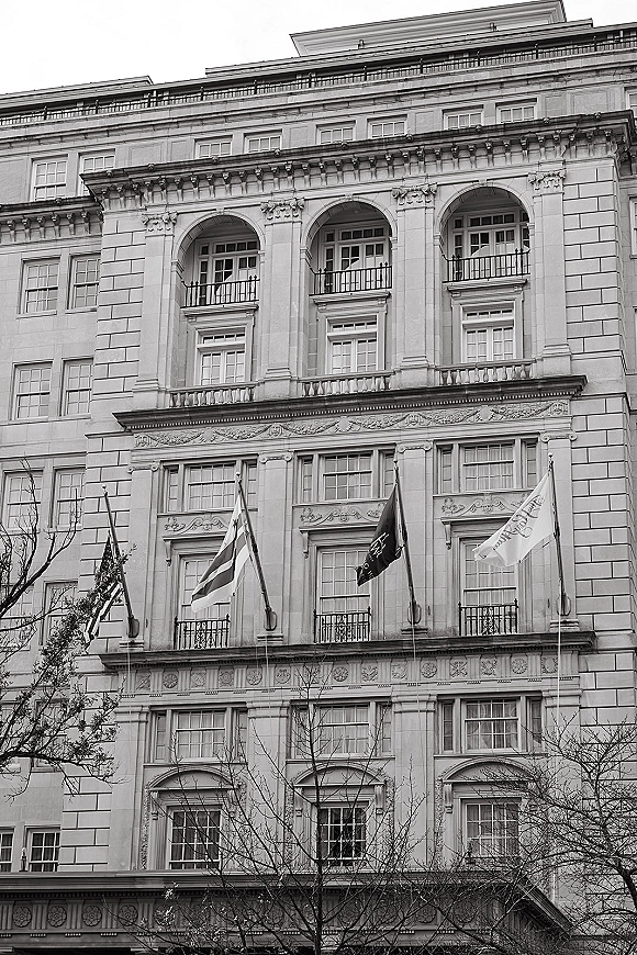 Wedding venue exterior of a hotel wedding venue with stone facade, arched windows, balconies, and flags beneath tree branches and sky