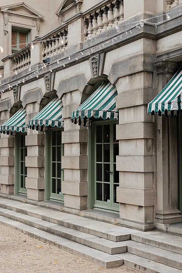 Wedding venue exterior with outdoor reception lighting and a striped awning, string lights above french doors on a classic stone facade courtyard