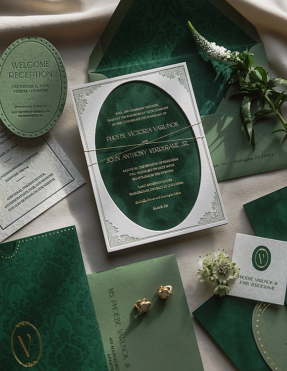 Wedding invitation suite with emerald green wedding invitations and gold foil lettering, wax-sealed envelopes, floral sprig on linen backdrop