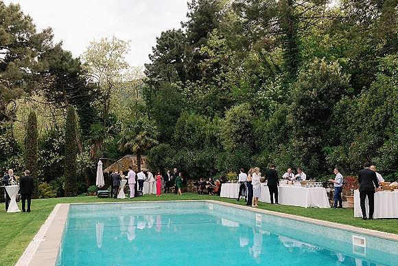 Cocktail hour reception poolside with white linen cocktail tables, bar glassware and ice buckets on the lawn beside the swimming pool