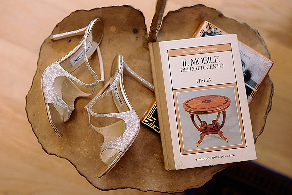 Wedding shoes and bridal heels in a flat lay of sparkly strappy silver sandals on books with a brass tray on a wood floor