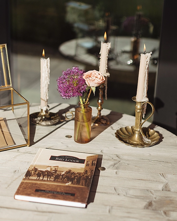 Wedding tablescape with brass candlestick centerpiece, taper candles and purple allium with blush rose in bud vase on a wood tabletop
