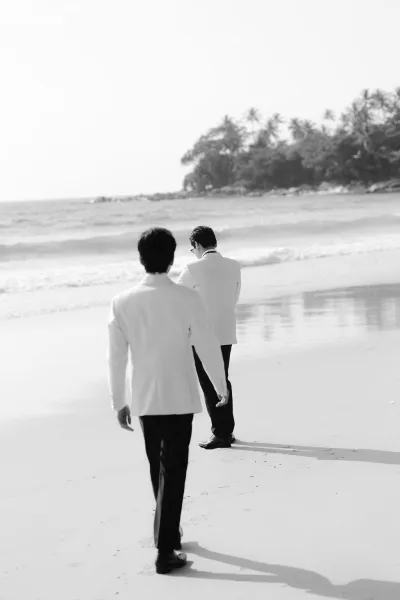 Beach wedding portrait, a black-and-white wedding photo of a groom in a white dinner jacket, strolling a palm-lined shore by rolling waves.