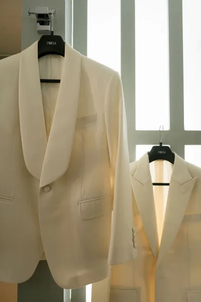 White tuxedo jacket on a hanger, styled as a white dinner jacket, set against window panes and wall panels.